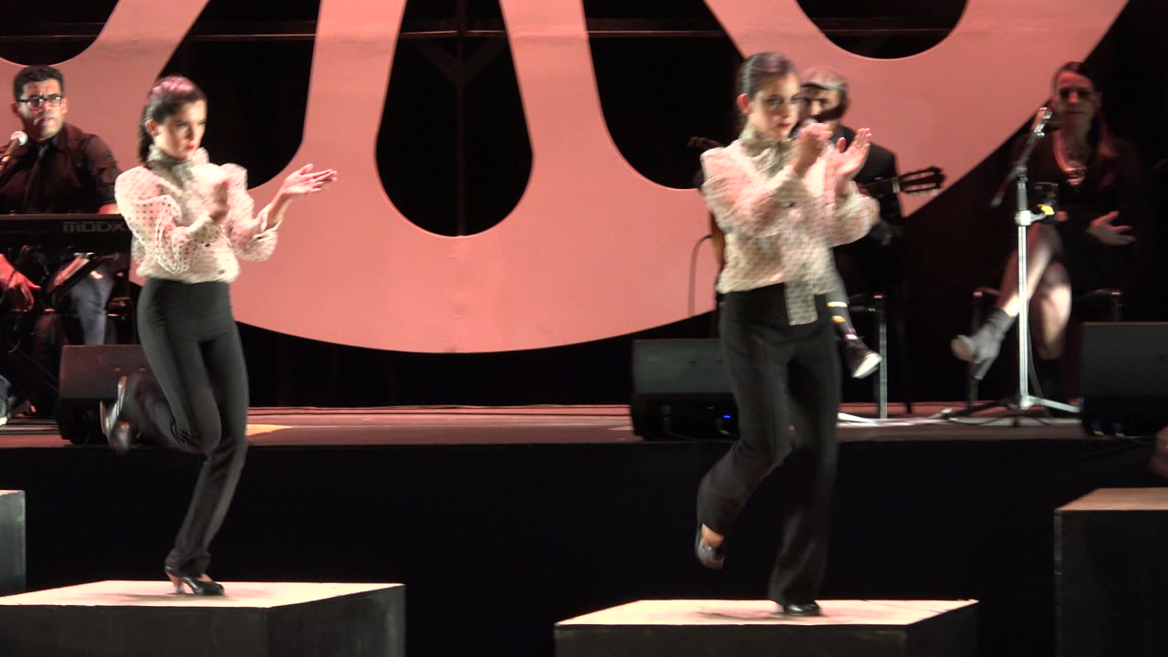 Two women dancing and clapping on stage blocks with musicians behind them.