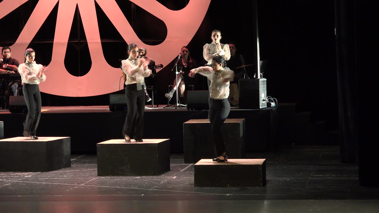 At 0:01, the Cabo San Lucas stage performance shows the center performer near a microphone while other women clap and move on separate black blocks.