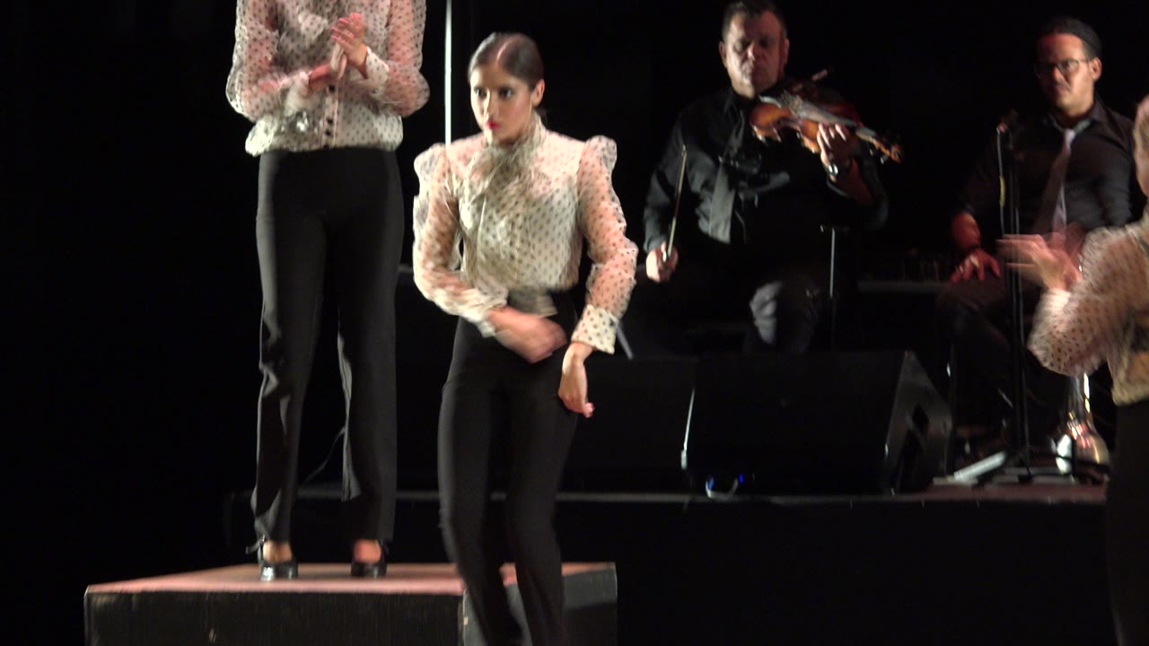 Girl stands forward on stage as another dancer claps behind her.