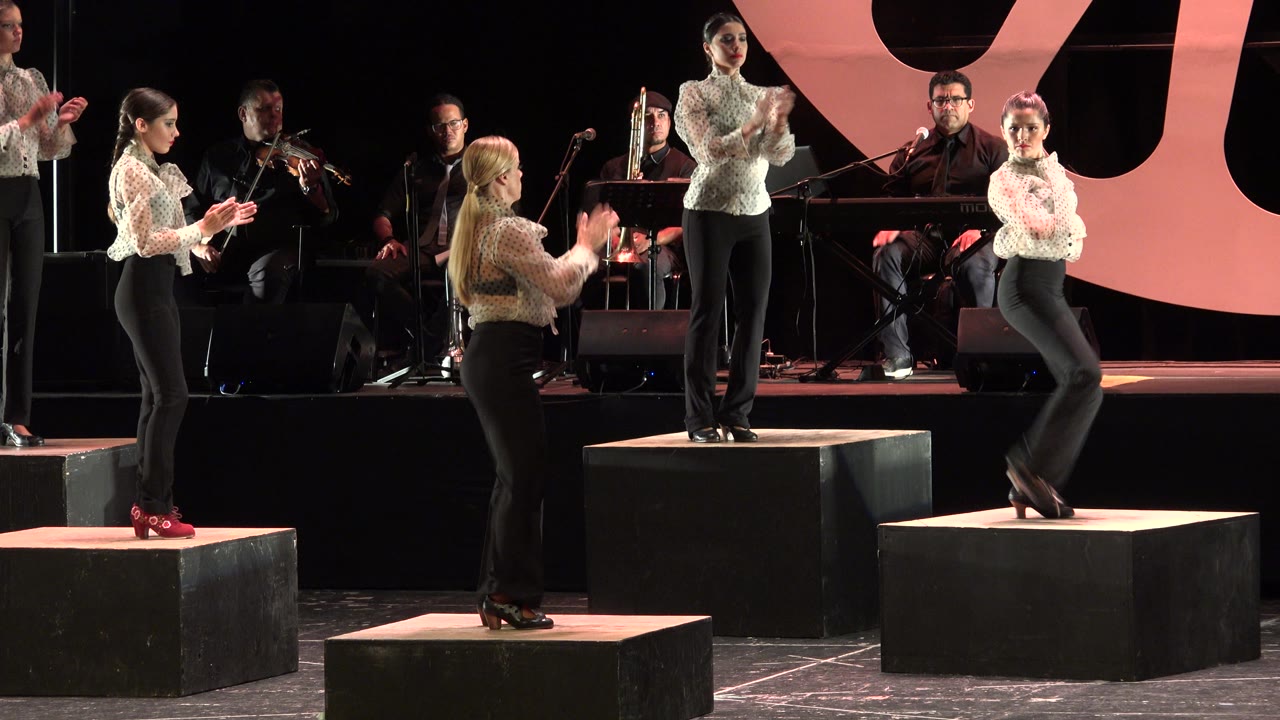 Women stepping and clapping on black risers under stage lighting.