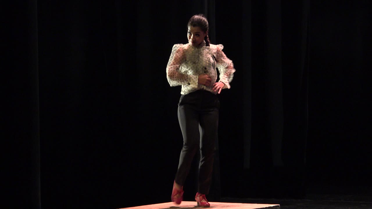 Young dancer standing on a lit stage box against black curtains.