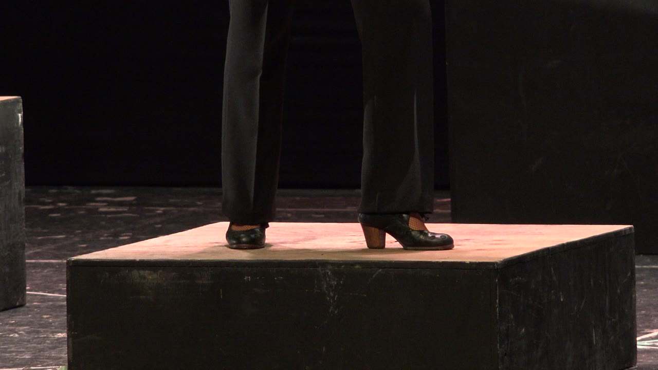 Close crop of adult performers' lower legs and black shoes standing on a raised black cube platform in Cabo San Lucas, Mexico.