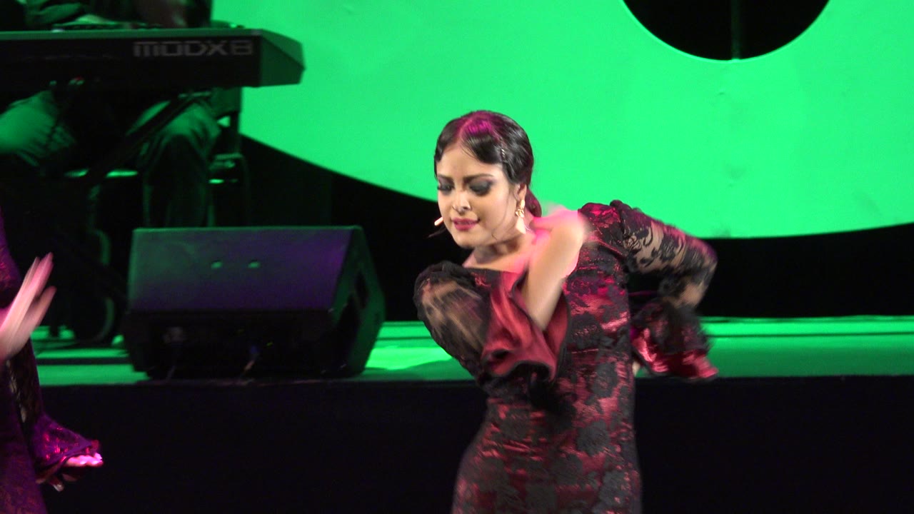 Female dancer in black lace costume bending forward on a green-lit stage.