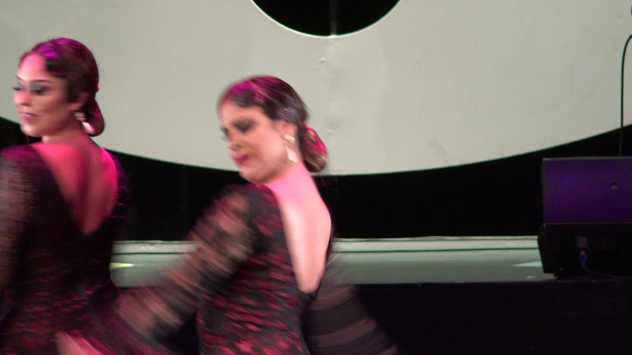 The two women continue the Cabo San Lucas stage performance, with one dancer facing partly away and the other moving her arms fast enough to blur.