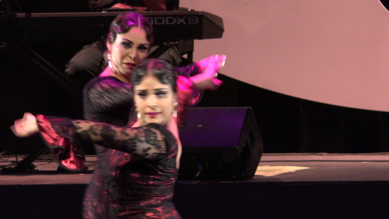 Two women dancing on a pink-lit stage with a keyboard behind them.