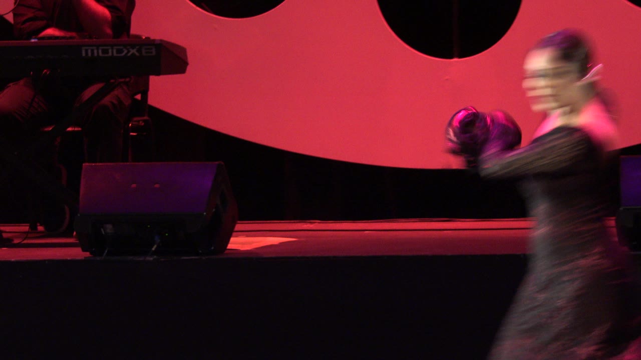 Blurred woman dancing across a red-lit stage with musicians behind her.