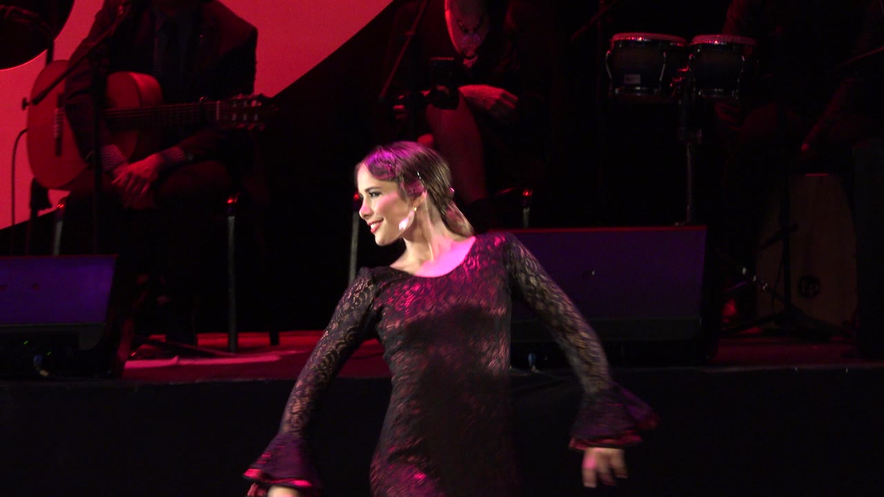 Woman in black lace dress dancing on a red-lit stage.