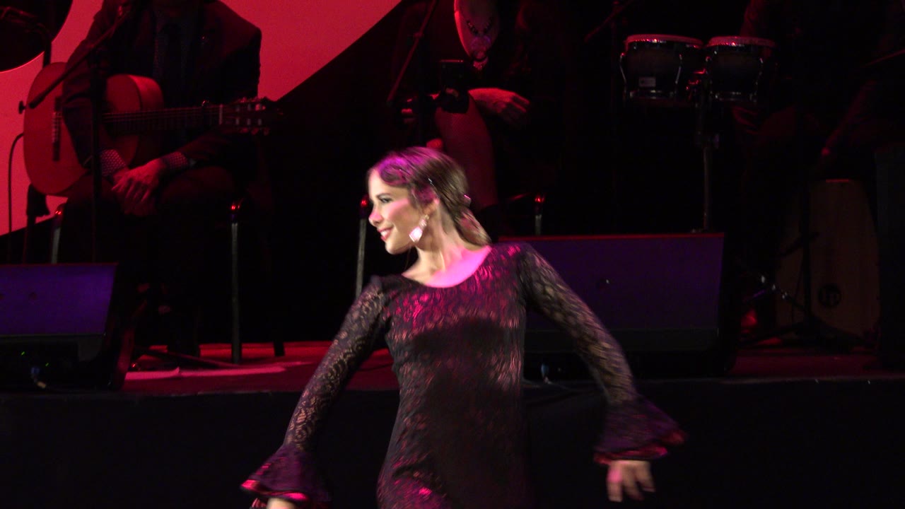 The performer continues across the stage in Cabo San Lucas, Mexico, with her face in profile, a dark band setup, and magenta light across her dress.