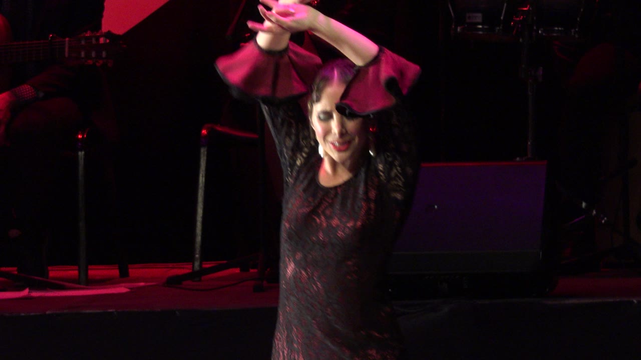 Woman dancing on a dark stage with arms raised.