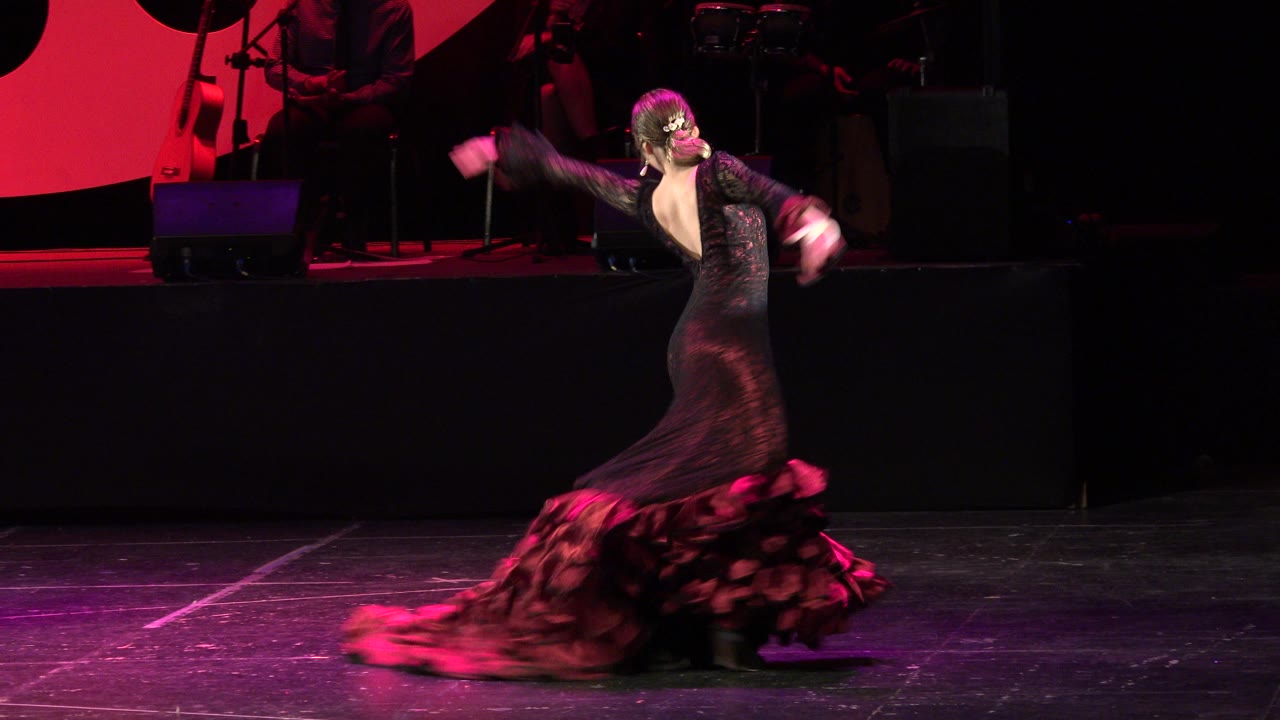 Dancer spinning on a dark stage under red lighting.