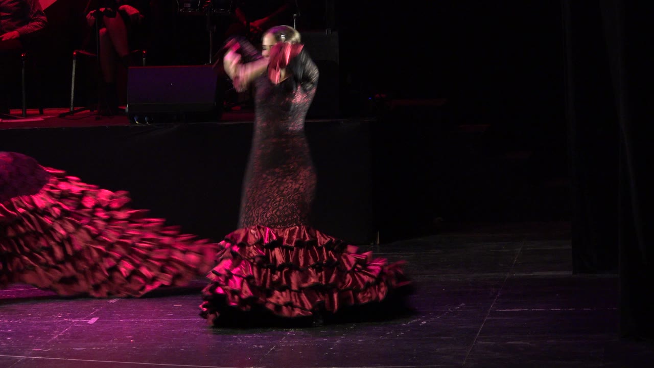 Woman in a black and red ruffled dress dancing on a dark stage.