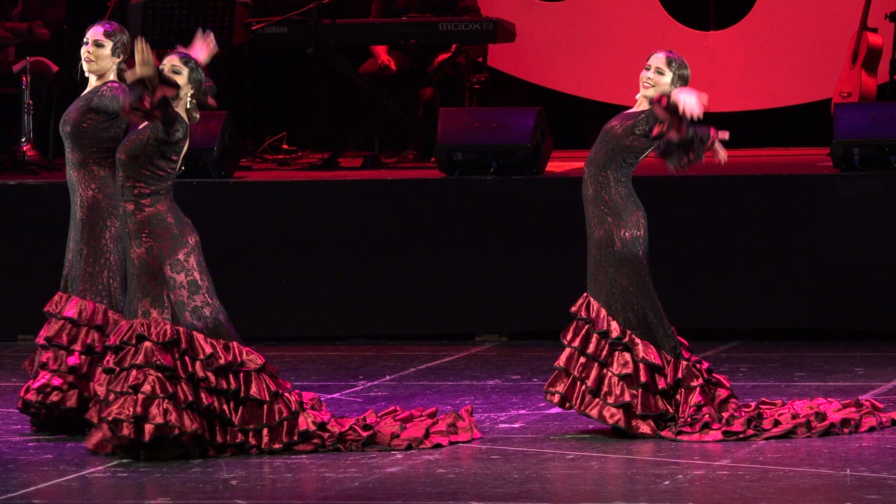 Two adult flamenco dancers in black and red dresses on a red-lit stage.