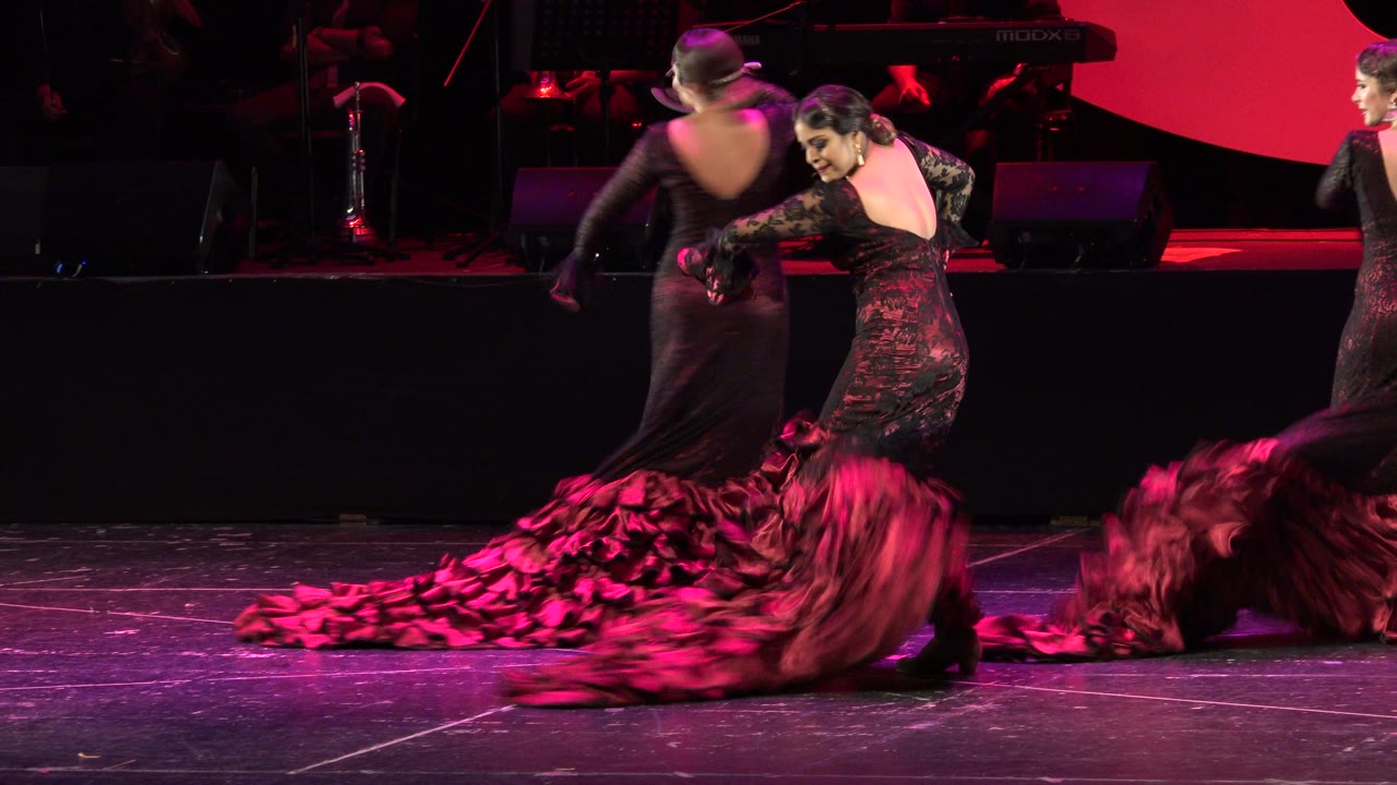 Black-dressed dancers turn as ruffled skirts sweep across the stage.