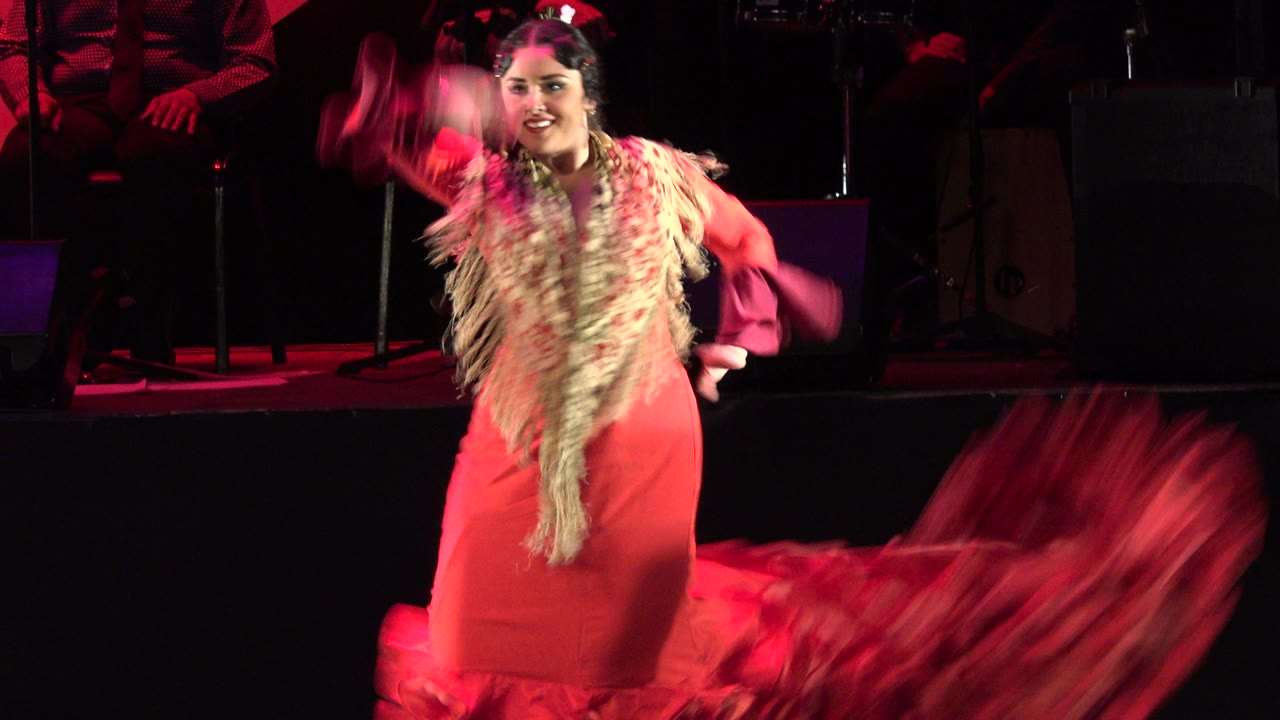 Woman in red dress facing forward with arm raised.
