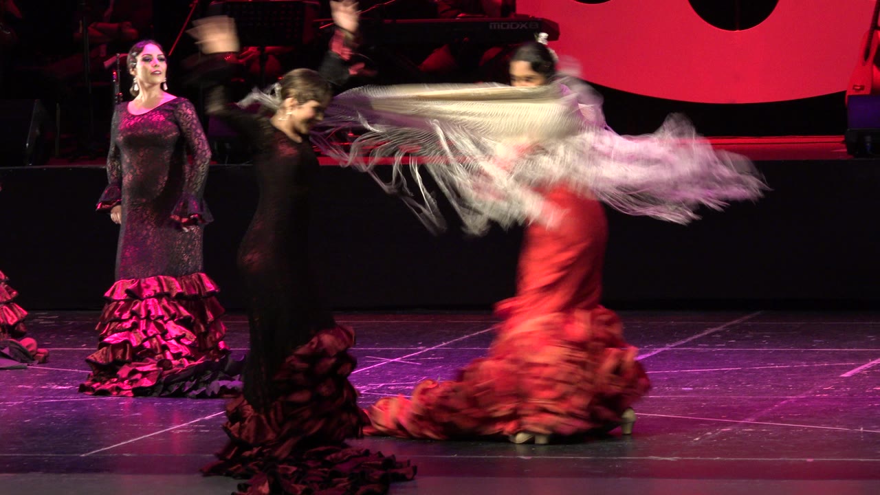 Flamenco dancers on a red-lit stage with a white shawl sweeping across the foreground.