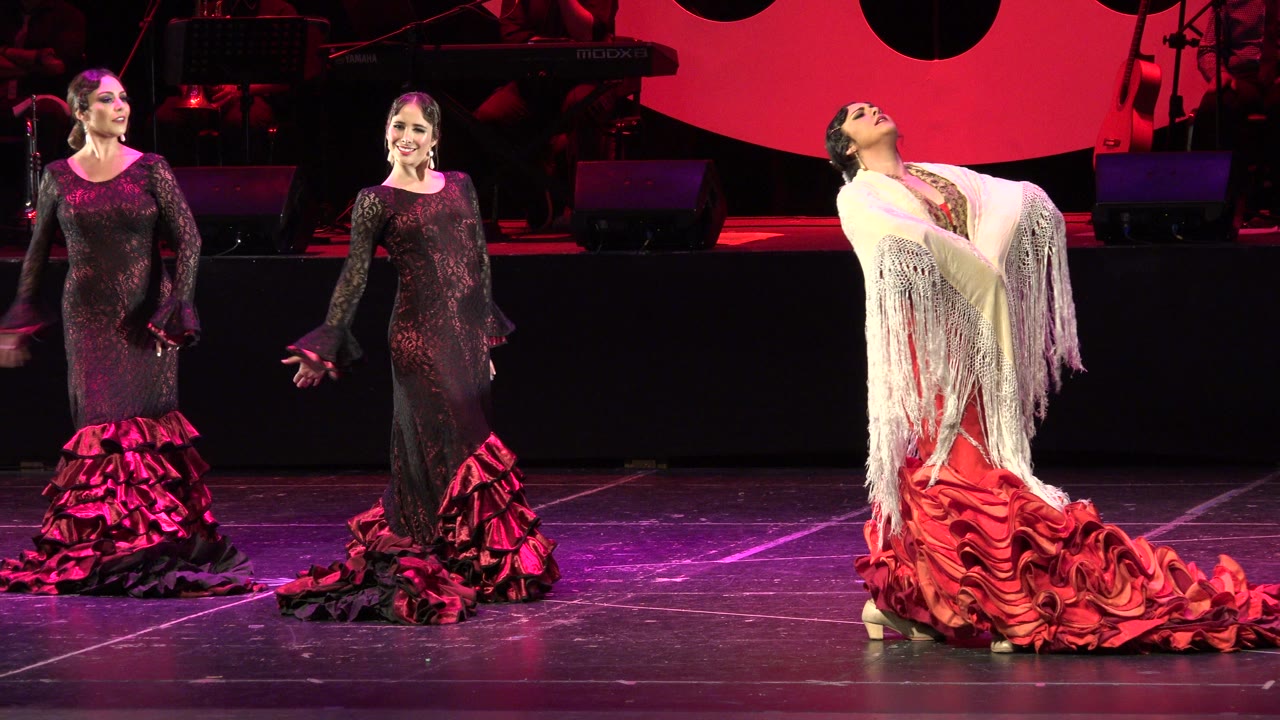 Three flamenco dancers on a red-lit stage.
