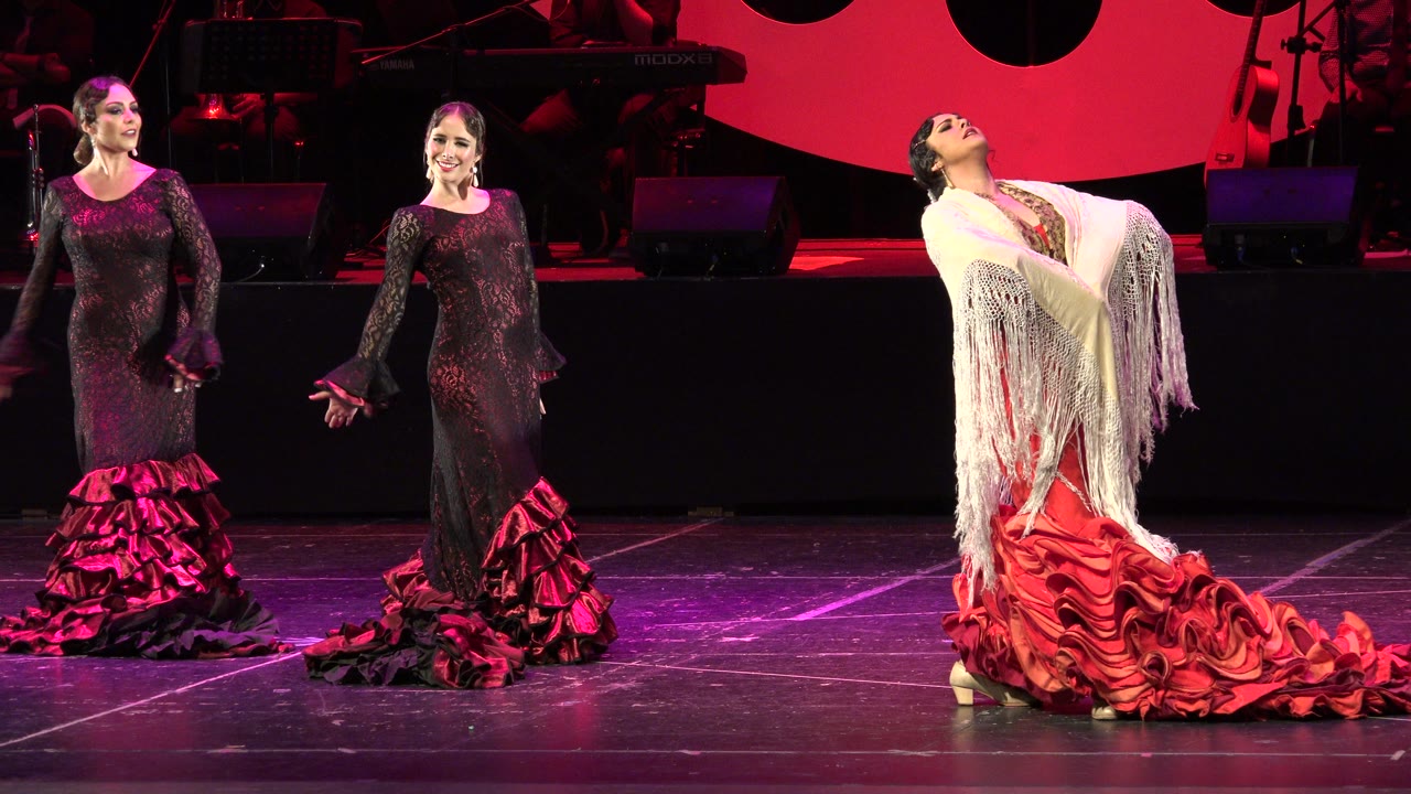 Two dancers in black ruffled flamenco dresses face the audience while the dancer in red leans back under a white fringed shawl on the Cabo San Lucas stage.
