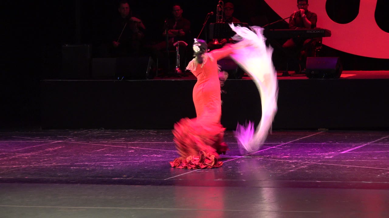 Woman in a red ruffled dress swings a white scarf on a dark stage.