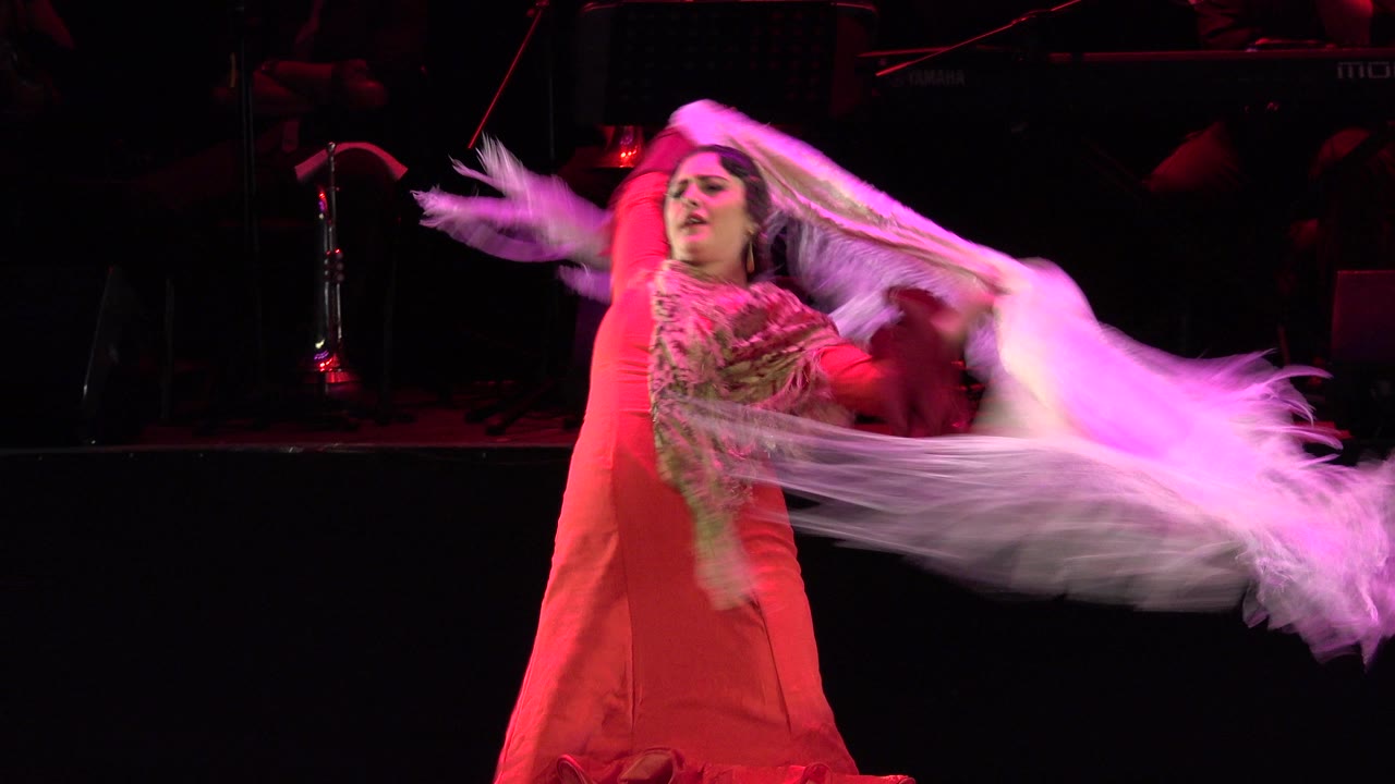 Woman in red dress swings a white fringed shawl on a dark stage.