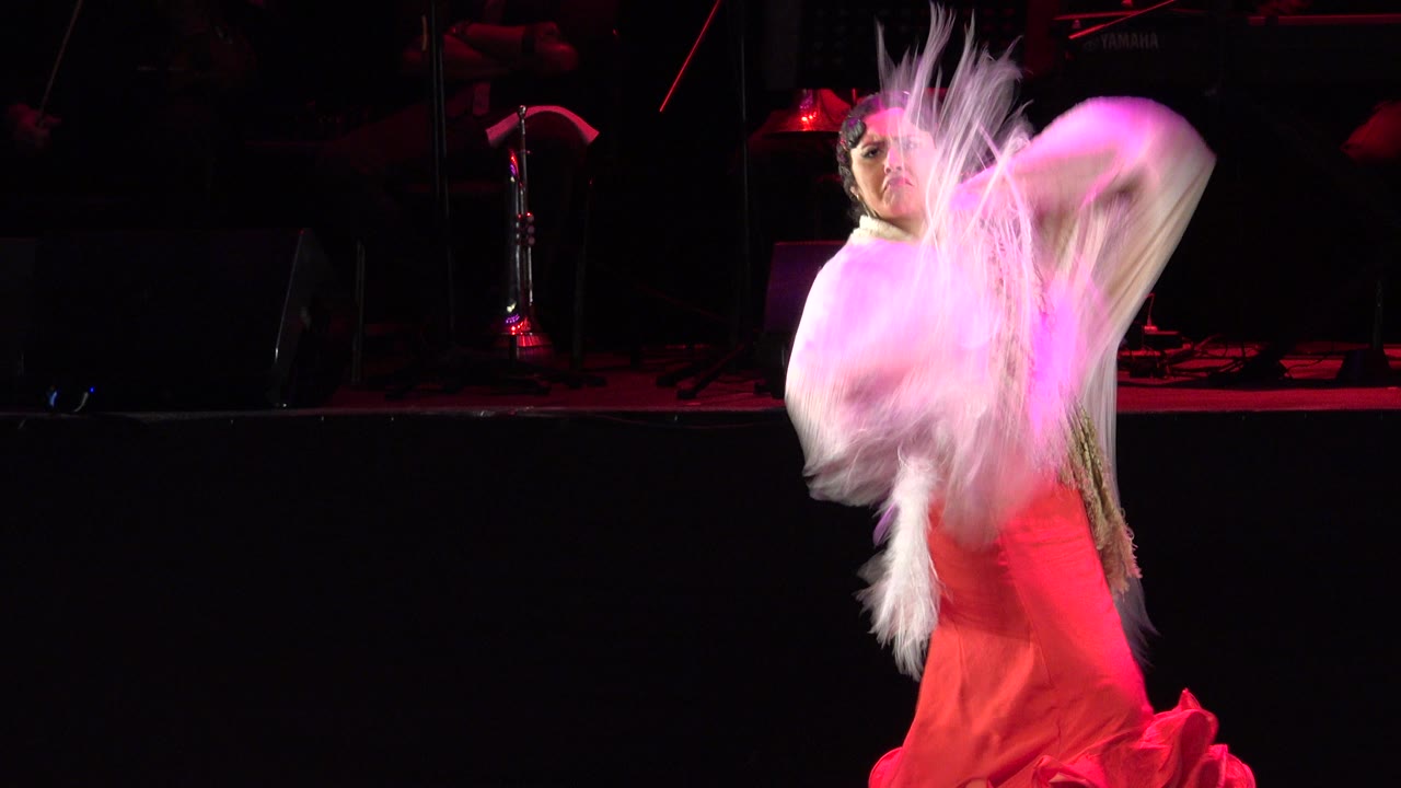 Woman in red gown swings a fringed shawl on a dark stage.