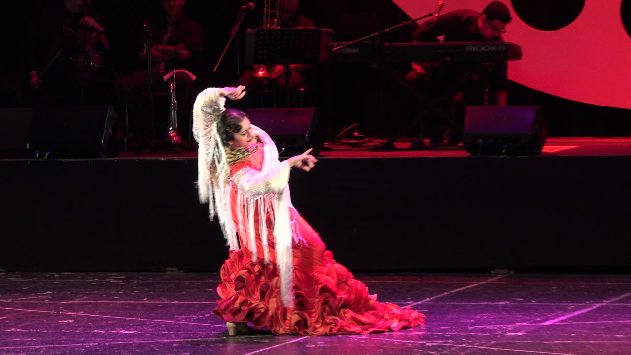 The dancer leans sideways with one arm lifted above her head and the other extended across her body during the Cabo San Lucas stage performance.
