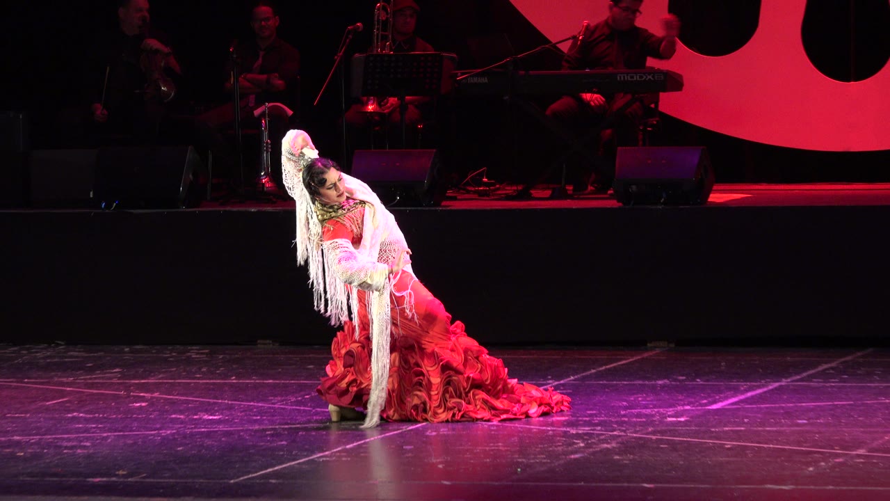 Dancer kneeling and leaning back in a red stage costume.