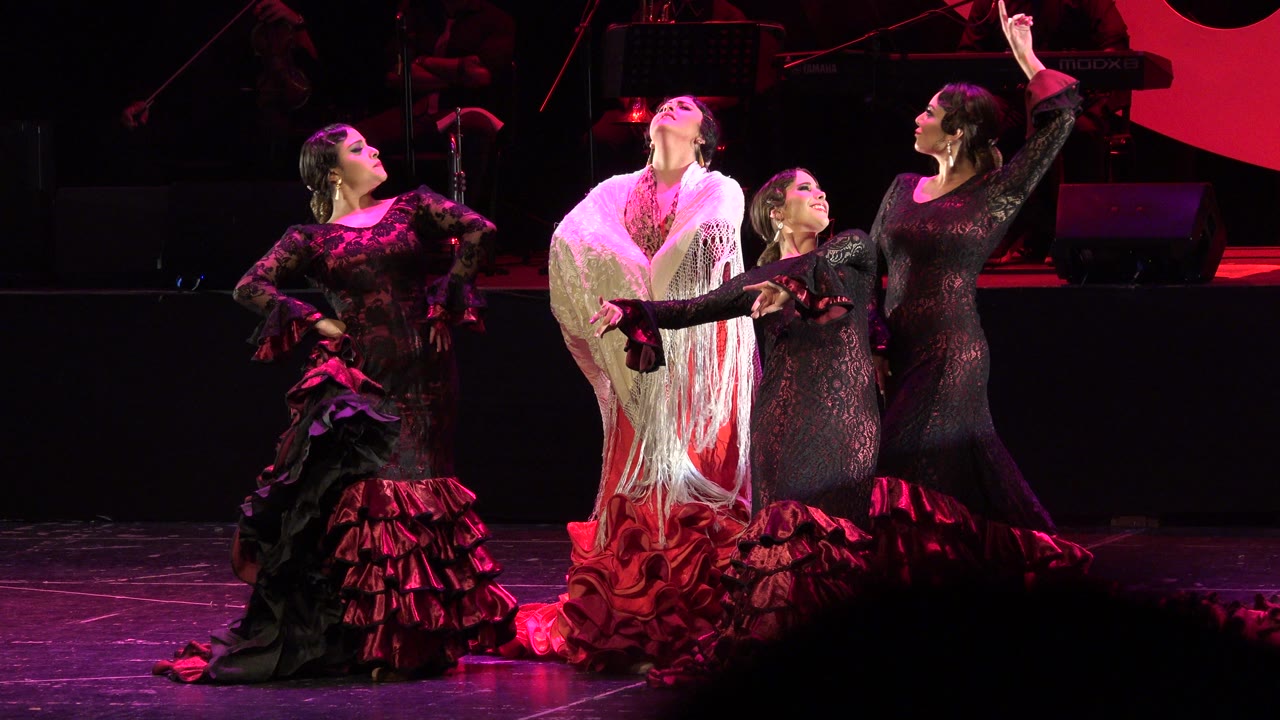 Four women in ruffled dance dresses posing on a red-lit stage.