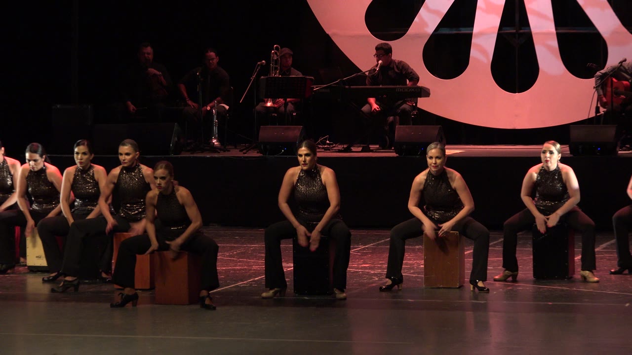 Adult women seated on stage with musicians behind them.
