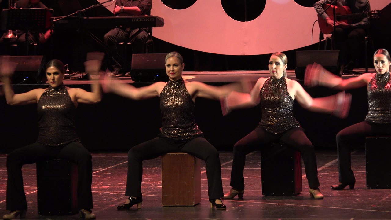 Three women dance seated on stage under red lighting.