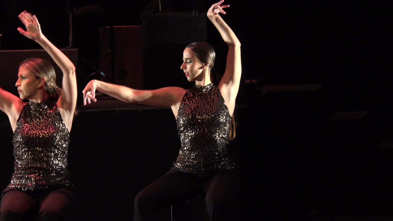 Two women in black sequined tops dancing on a dark stage.