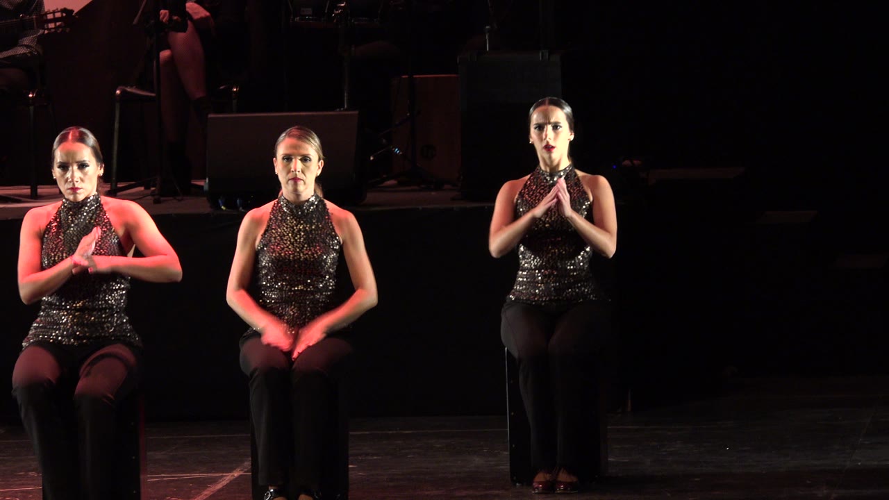 Three seated dancers hold rounded arm shapes above their heads.