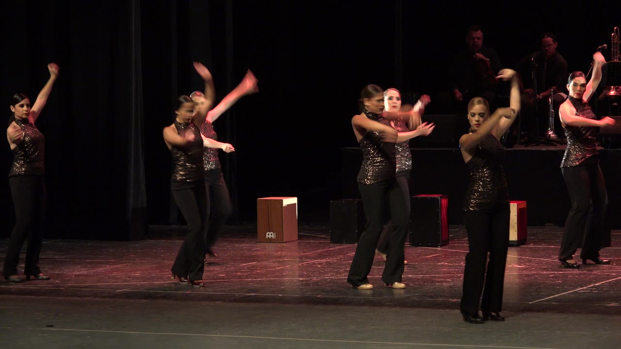 Women in black dance outfits performing on a dark stage.