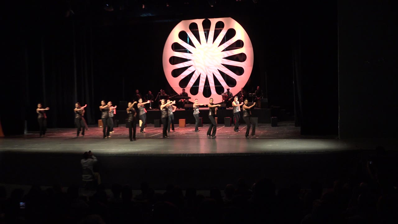Wide Cabo San Lucas performance frame with the ensemble centered on stage, dark curtains around them, and the illuminated circular backdrop dominating the background.