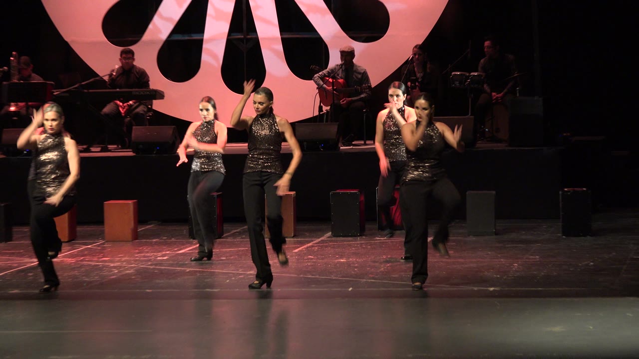 Four dancers perform on a stage with musicians behind them.