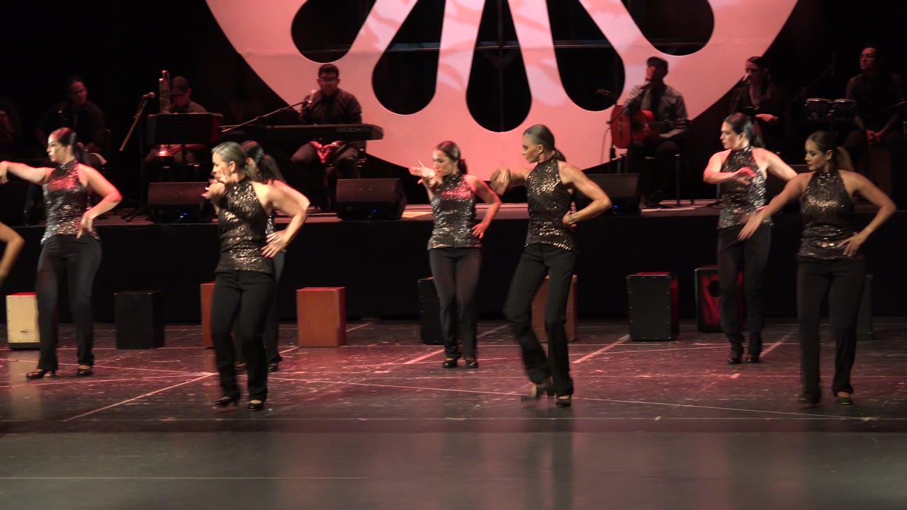 At 0:01, the dancers hold a similar stage formation in Cabo San Lucas, Mexico, with one performer stepping forward while the band remains in shadow behind them.