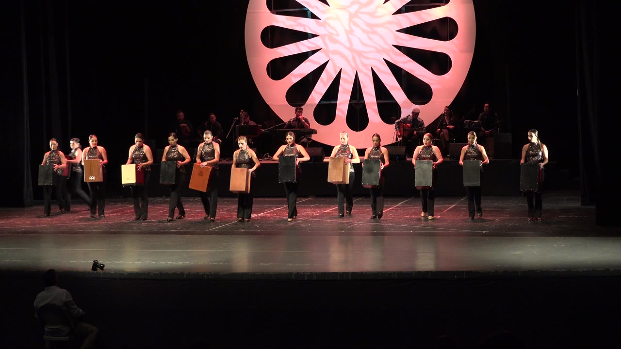 Women stand in a row on a stage holding wooden boxes.