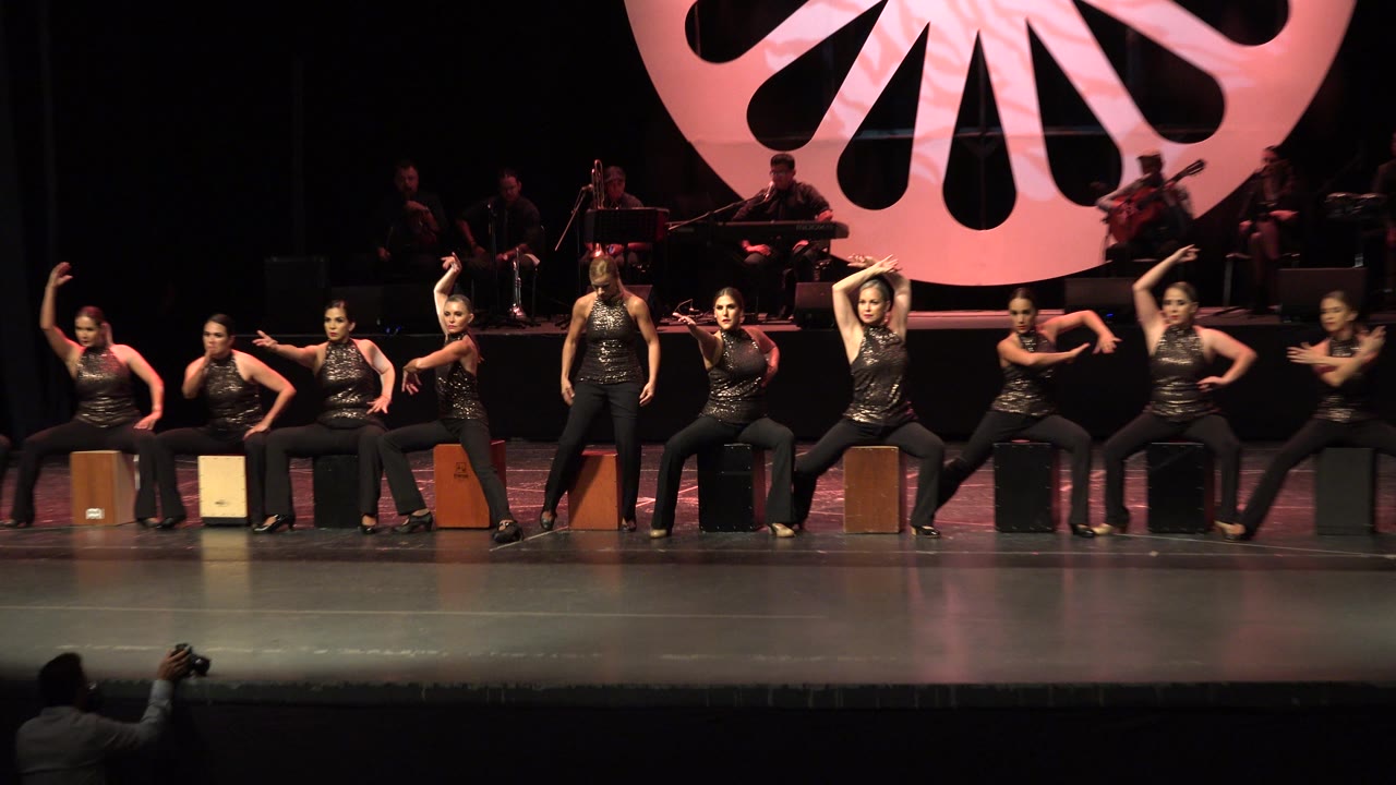 Wide stage view with seated performers and a person photographing near the foreground.