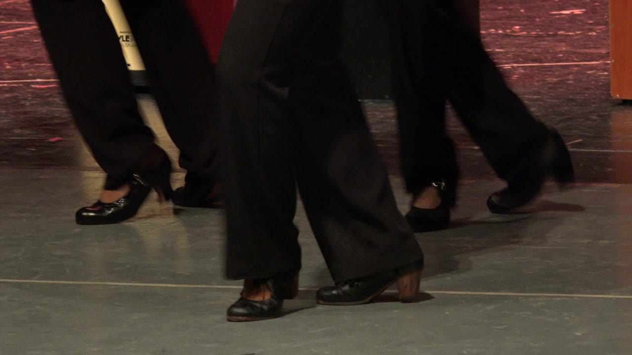 Dancers' feet crossing on a gray stage floor.