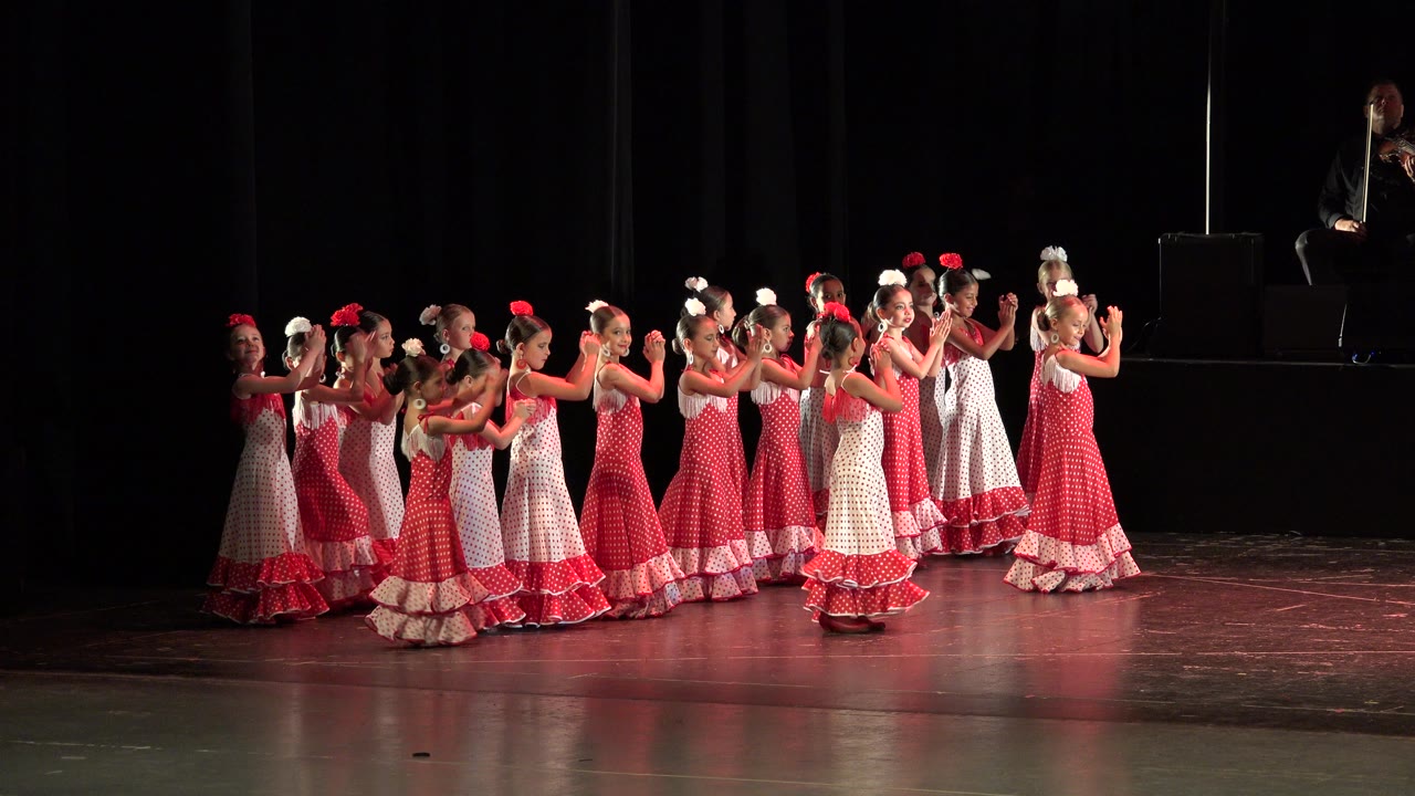 Children in red and white dresses clapping on a dark stage.