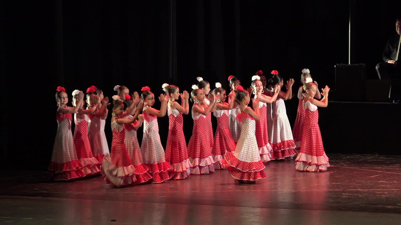 Girls in red and white ruffled dresses dancing on a dark stage.