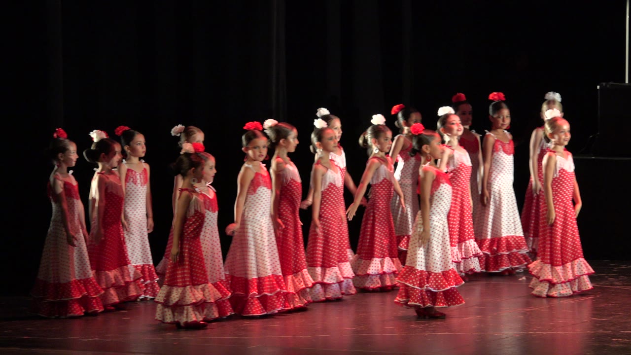 Girls in red and white dresses lined up on a dark stage.