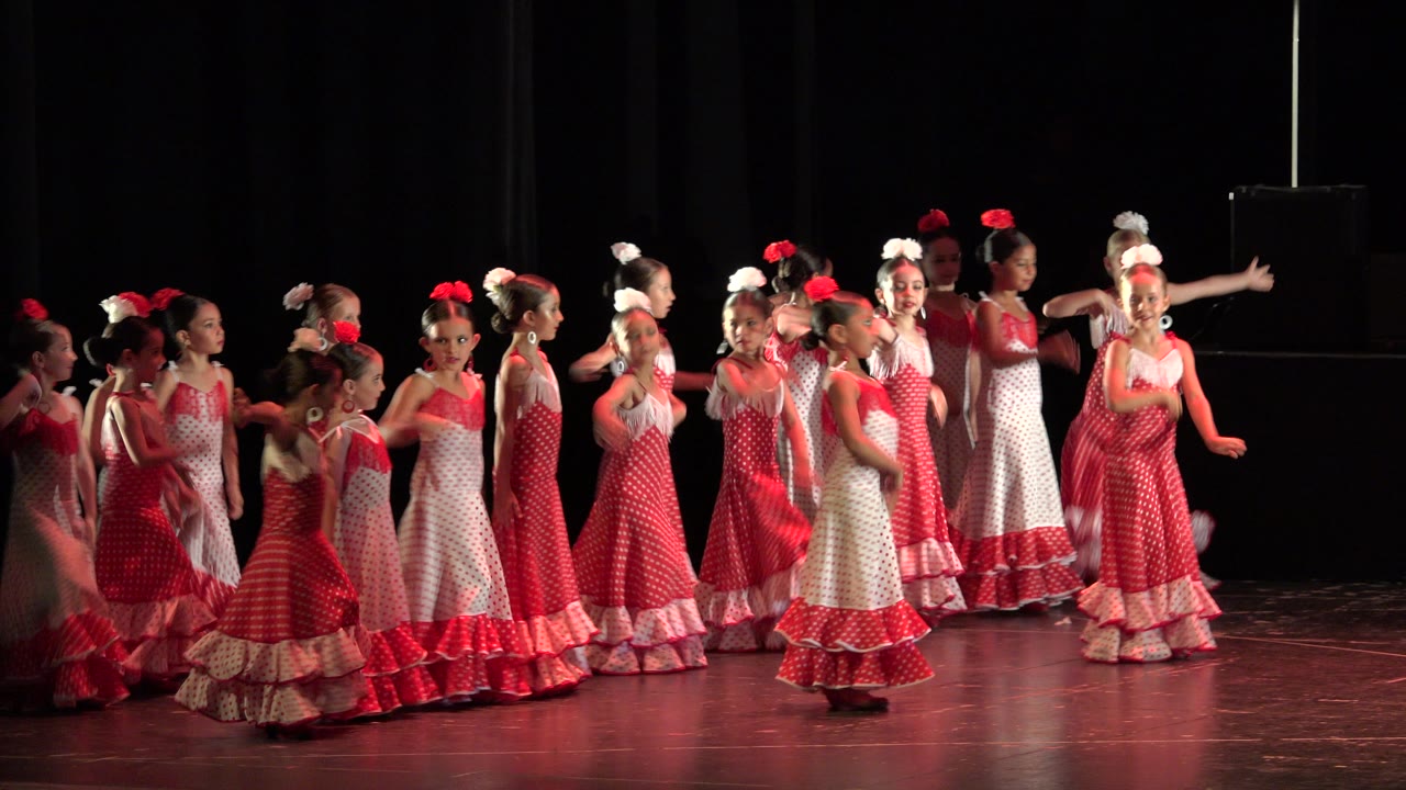 Girls in red dresses begin moving with arms raised on stage.