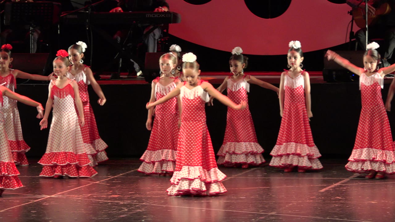Girls in red dresses shift formation during a stage routine.