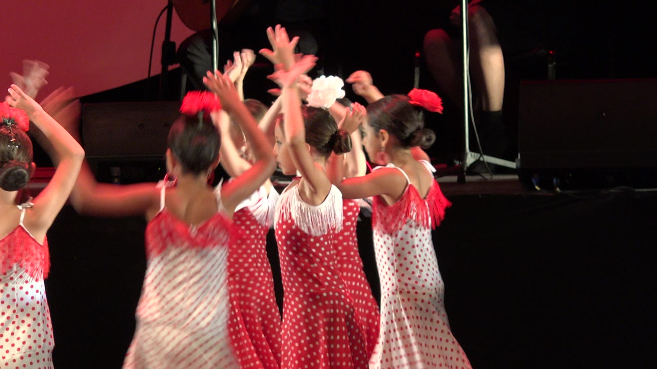Young girls in red and white dresses raise their arms on stage.
