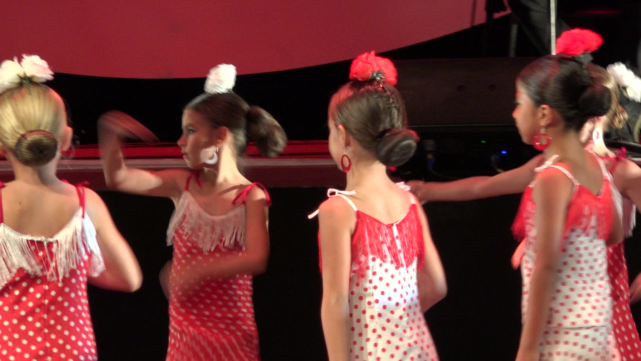 Young girls in red and white costumes dancing on a dark stage.