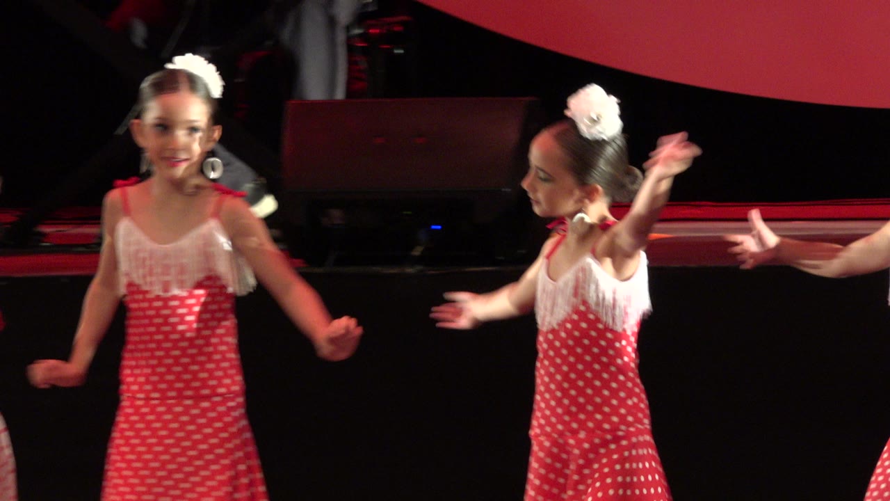 Two girls in red and white dance dresses on a dark stage.