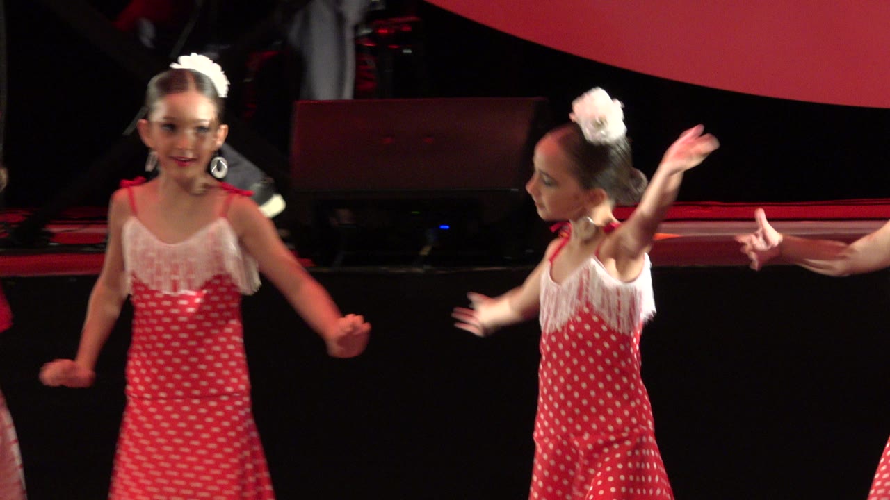 Two young dancers remain near the front of the stage in Cabo San Lucas, Mexico, with one girl looking toward camera while another gestures to the side.