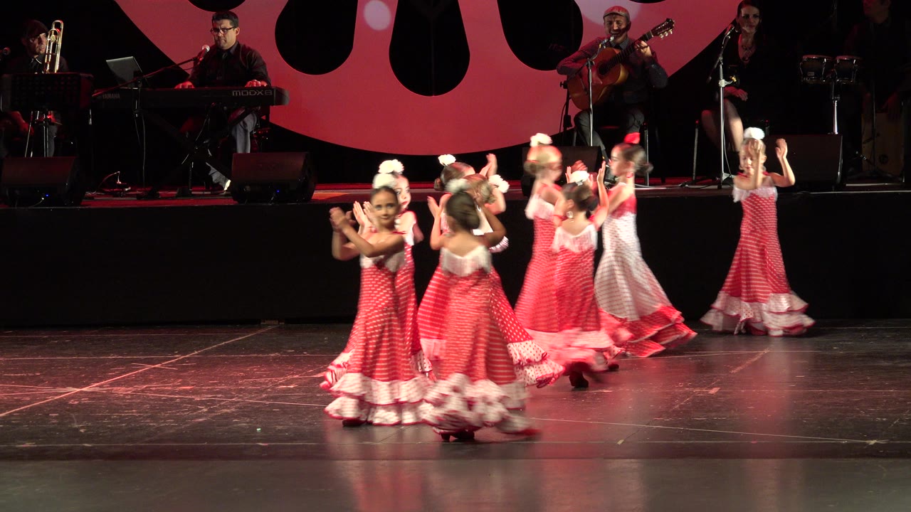 One second in, the Cabo San Lucas dance group gathers near center stage with hands raised and dresses flaring as the band remains seated behind them.