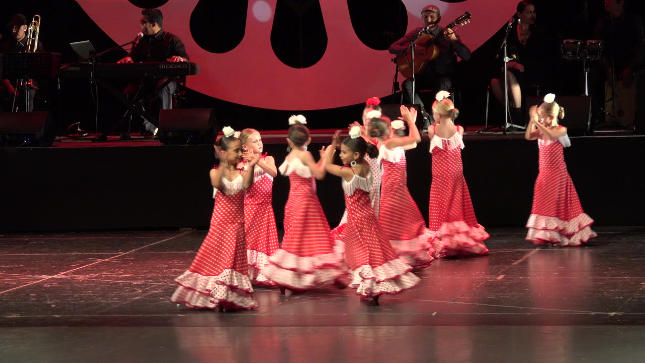 Children in matching red dresses dance in pairs across the stage.