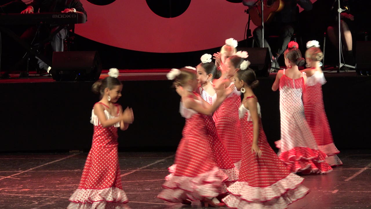 Young girls in red and white dresses clap and move on a stage.